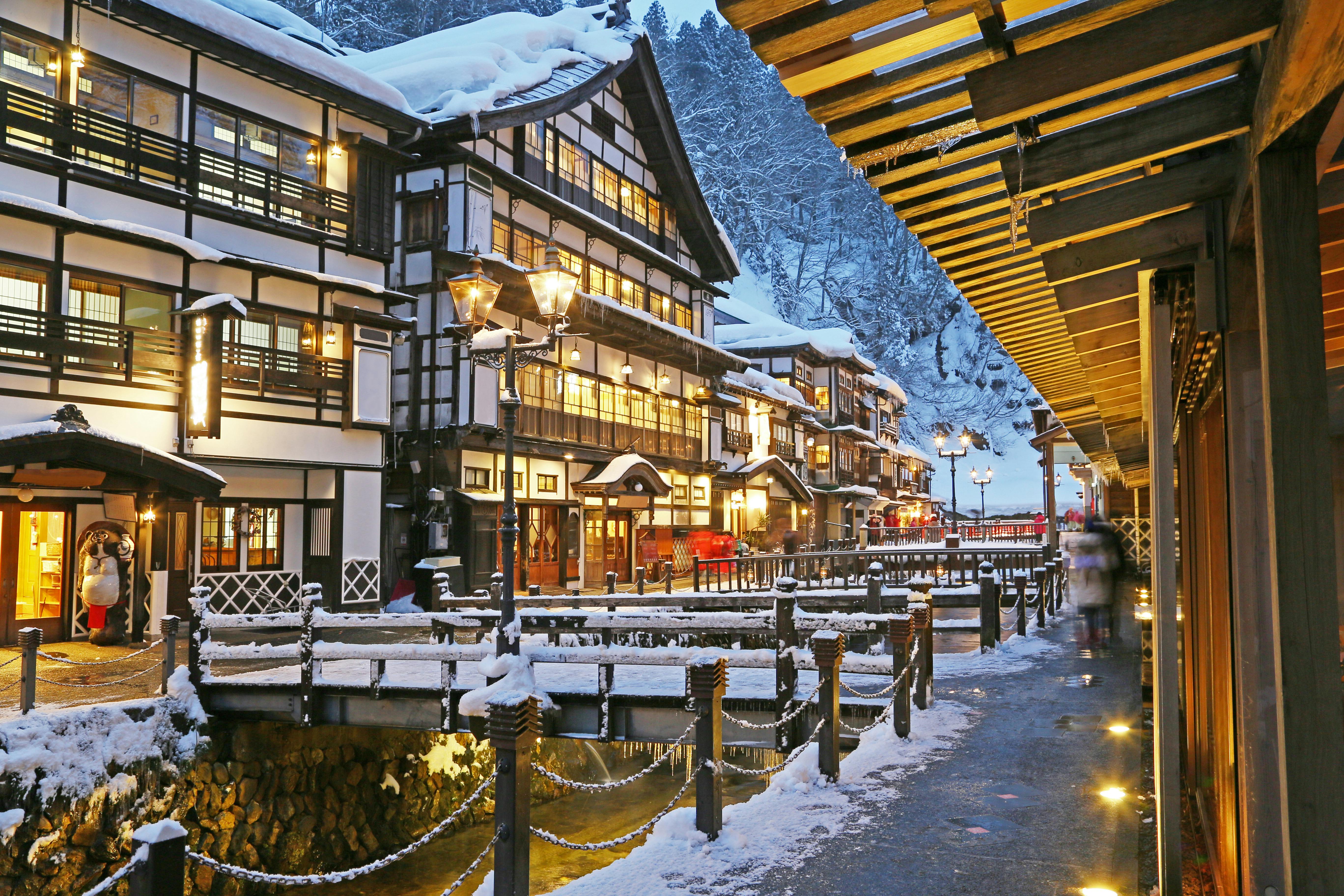 Ginzan Onsen in yamagata, Japan - A fairytale hot spring village with traditional multi-story wooden ryokan lining a snowy valley, featuring gas lanterns, foot baths, and nostalgic Taisho-era atmosphere.